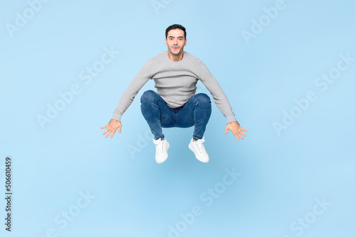 Energetic fun handsome young Caucasian man jumping like a frog in light blue color isolated studio background
