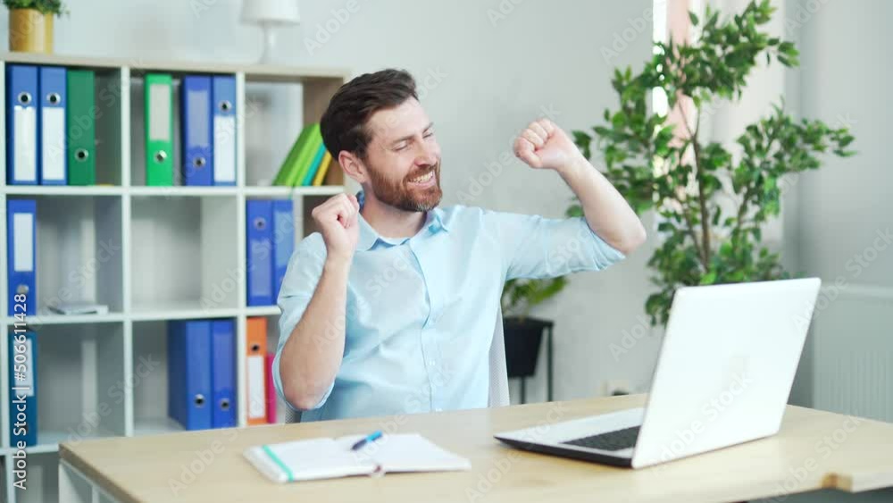 Happy and cheerful office worker dancing at work sitting at a computer desk. enjoy after successful agreement. employee business man in shirt Handsome funny Bearded Manager rejoices in the work done Happy and cheerful office worker dancing at work sitting at a computer desk. enjoy after successful agreement. employee business man in shirt Handsome funny Bearded Manager rejoices in the work done