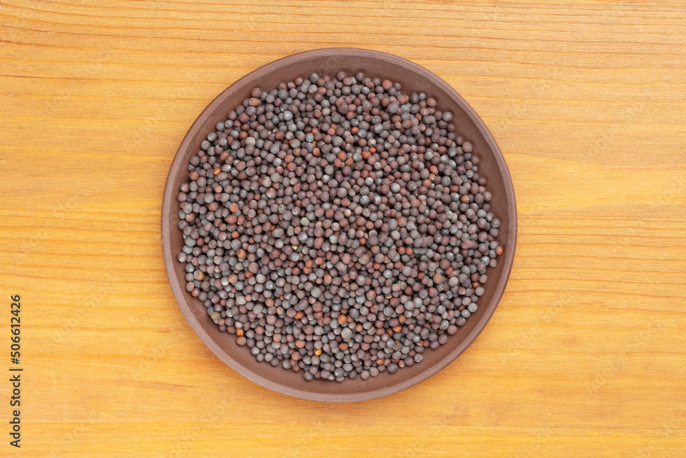 Spice Mustard seeds (Brassica juncea) in brown clay plate on yellow wooden background. Close up. Vegetarian food concept Spice Mustard seeds (Brassica juncea) in brown clay plate on yellow wooden background. Close up. Vegetarian food concept