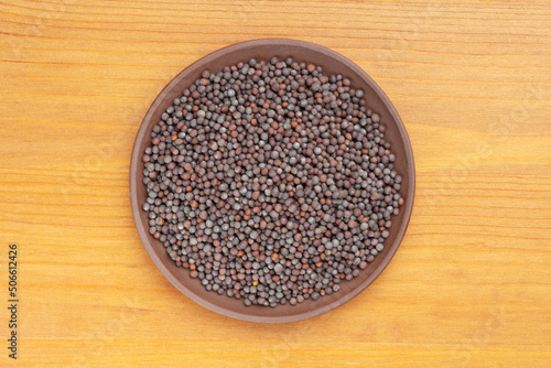 Spice Mustard seeds (Brassica juncea) in brown clay plate on yellow wooden background. Close up. Vegetarian food concept