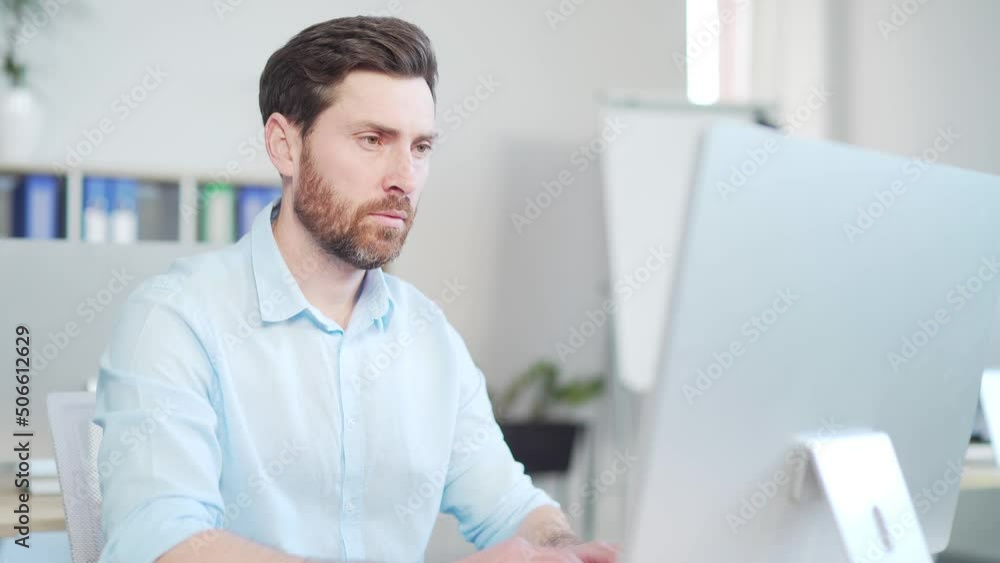 Focused confident handsome bearded business man looks at screen computer monitor or laptop at work in the office. Close up of thoughtful employee entrepreneur in smart casual browsing typing Indoor Focused confident handsome bearded business man looks at screen computer monitor or laptop at work in the office. Close up of thoughtful employee entrepreneur in smart casual browsing typing Indoor