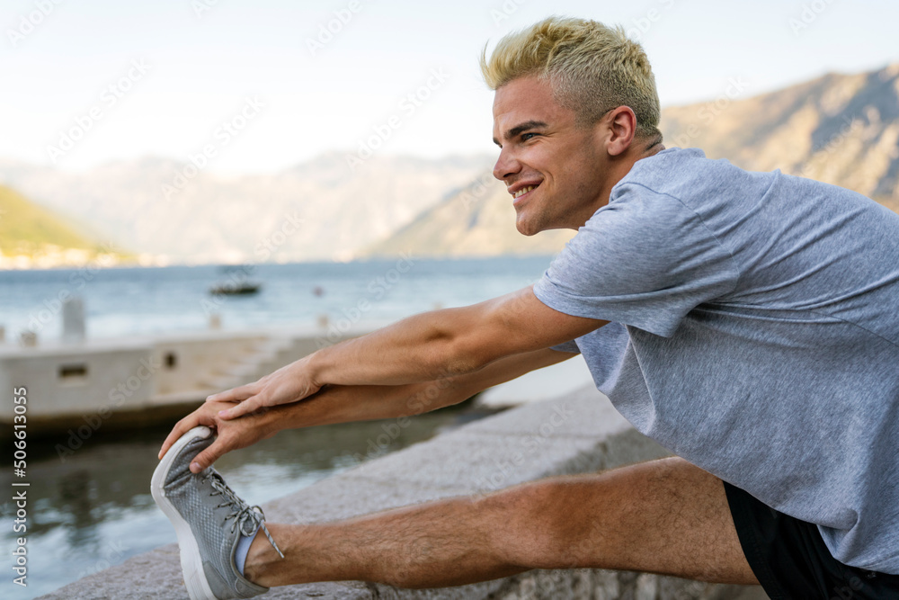Athletic male runner doing stretching exercise, preparing for morning workout outdoors