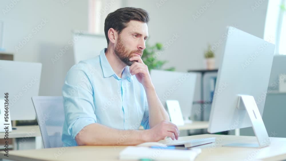 Focused bearded business man entrepreneur typing on laptop pc computer doing research. Young male professional using computer sitting at modern office desk. Busy worker working on modern tech notebook