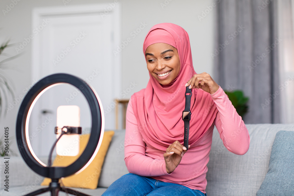 Excited muslim lady blogger recording video review of new smartwatch model, using ring lamp and smartphone at home - obrazy, fototapety, plakaty 