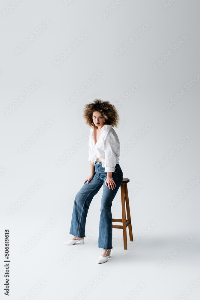 Stylish model in blouse posing near chair on white background.