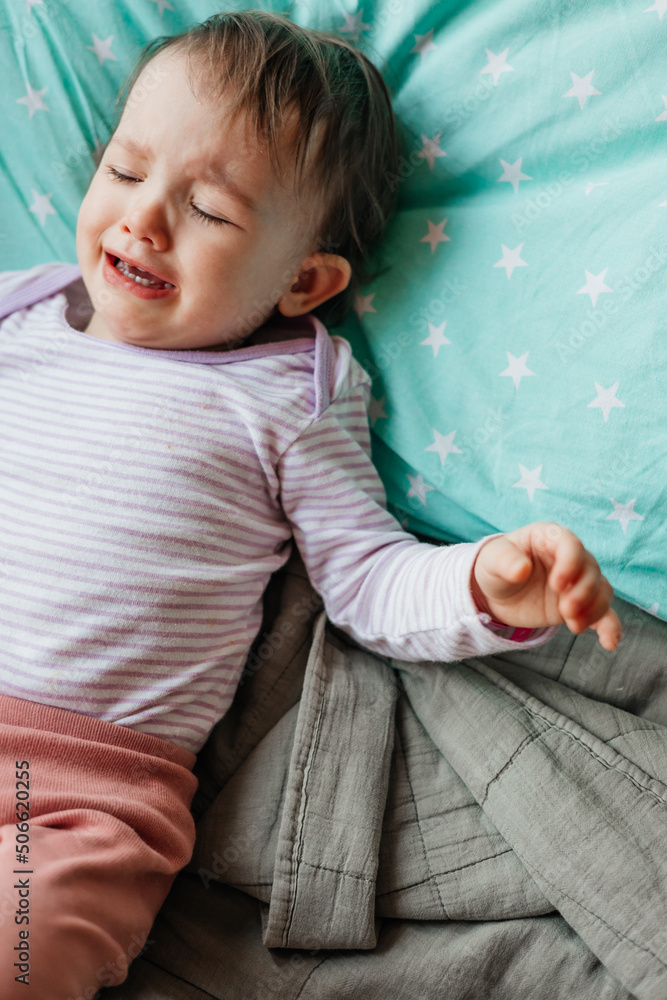Fototapeta premium a child with a catheter in his hand cries a lot and cries while lying in bed in the hospital
