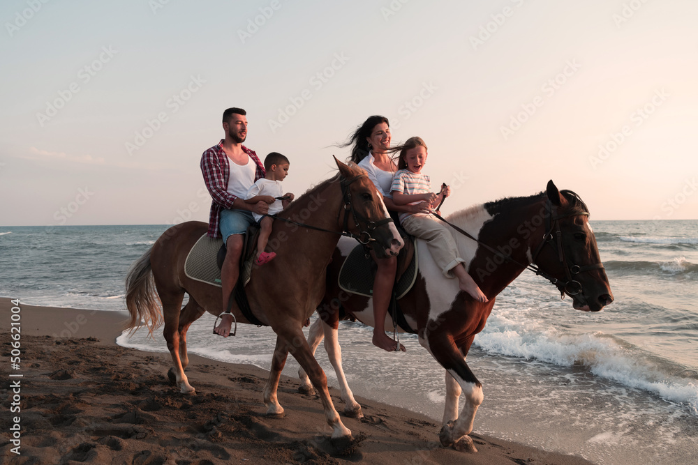 The family spends time with their children while riding horses together on a sandy beach. Selective focus The family spends time with their children while riding horses together on a sandy beach. Selective focus