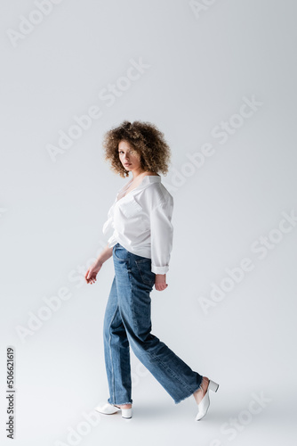 Trendy woman in jeans walking on white background.