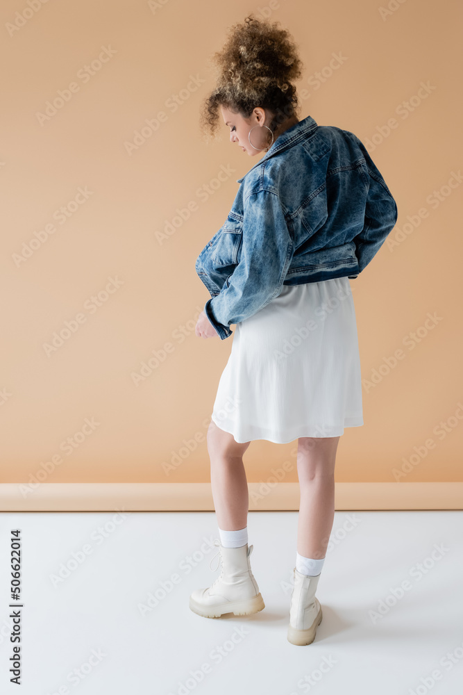 Side view of curly woman in denim jacket and boots on beige background. Side view of curly woman in denim jacket and boots on beige background.