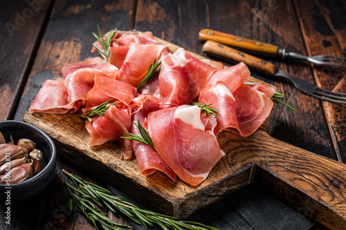 Slices of jamon serrano ham or prosciutto crudo parma on wooden board with rosemary. Wooden background. Top view