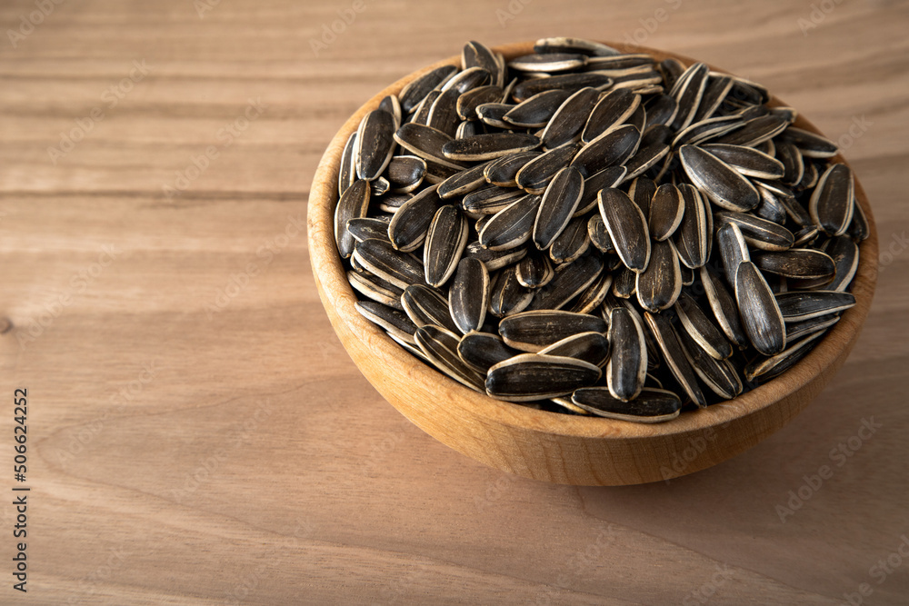 Black sunflower seeds in a bowl on wooden background Black sunflower seeds in a bowl on wooden background