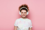 Smiling woman in t-shirt and headphones isolated on pink.