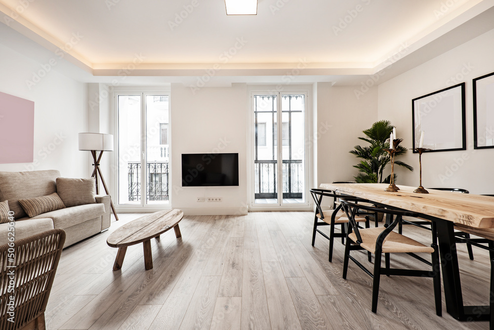 Fototapeta premium Living room with raw wood side table, wood plank dining table, matching rattan and black wood chairs and metal and glass windows