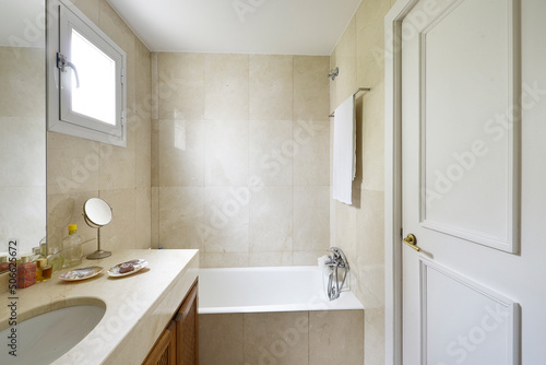 Toilet with shower cabin  cream-colored marble tiles and countertop with a white sink on wooden cabinet with grids