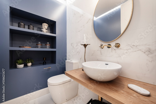 Designer toilet with half circle porcelain sink on light wood countertop and ornate shelving on blue wall