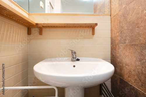 small cloakroom with white porcelain sink with wooden shelves and matching framed mirror