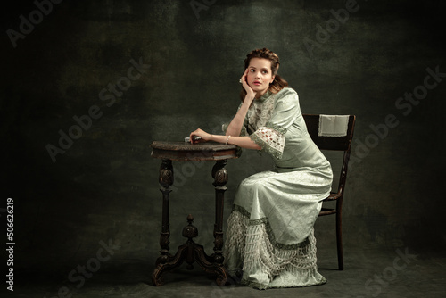 Vintage portrait of young beautiful girl in gray dress of medieval style isolated on dark background. Comparison of eras concept, flemish style. Art, beauty photo