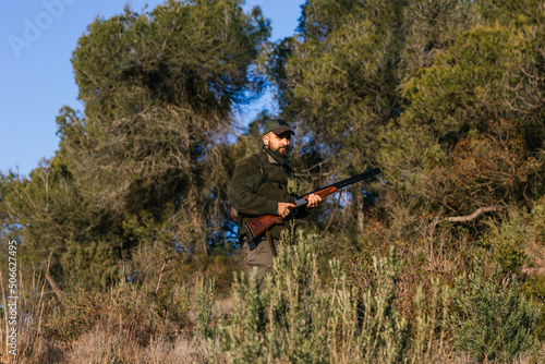 Hunter walking among outdoor grass with gun