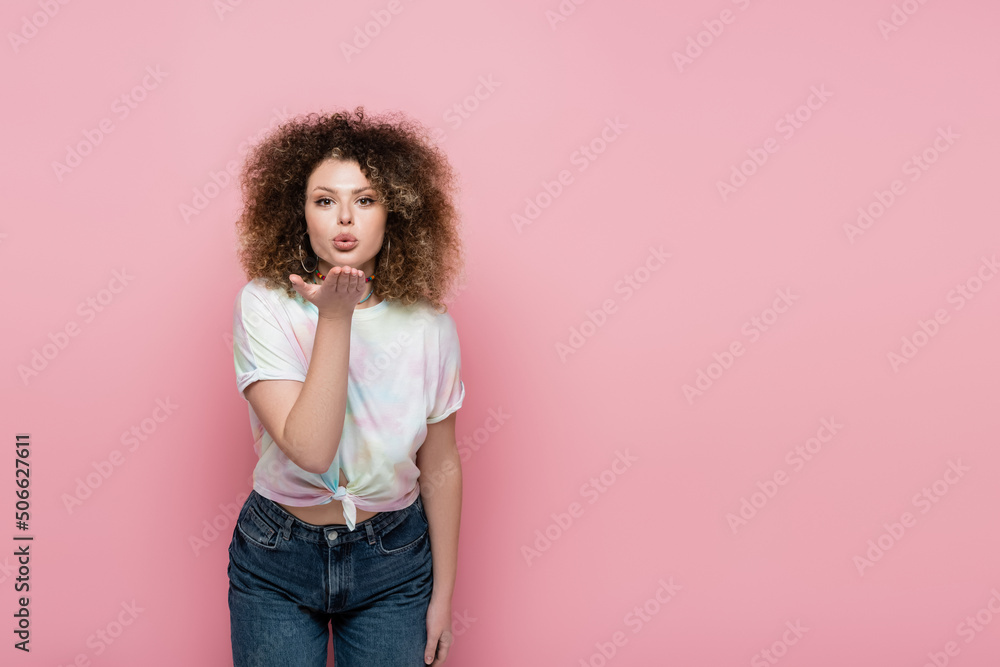 Curly woman blowing air kiss at camera isolated on pink. Curly woman blowing air kiss at camera isolated on pink.
