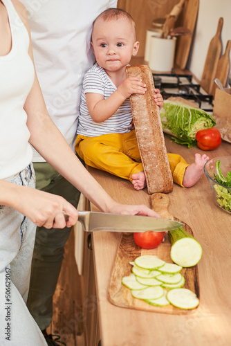 A boy toddler with his parents in the kitchen prepares together a fresh healthy salad.