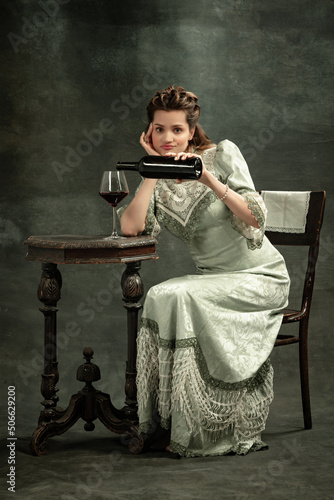 Conceptual portrait of young charming girl in image of medieval royal person or viscountess posing isolated on dark background. Comparison of eras concept. Modern art, beauty photo