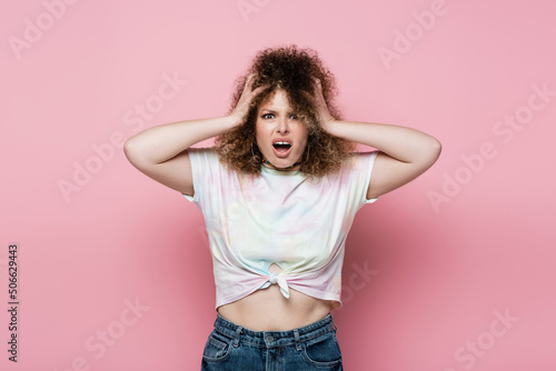 Stressed woman in t-shirt screaming on pink background.