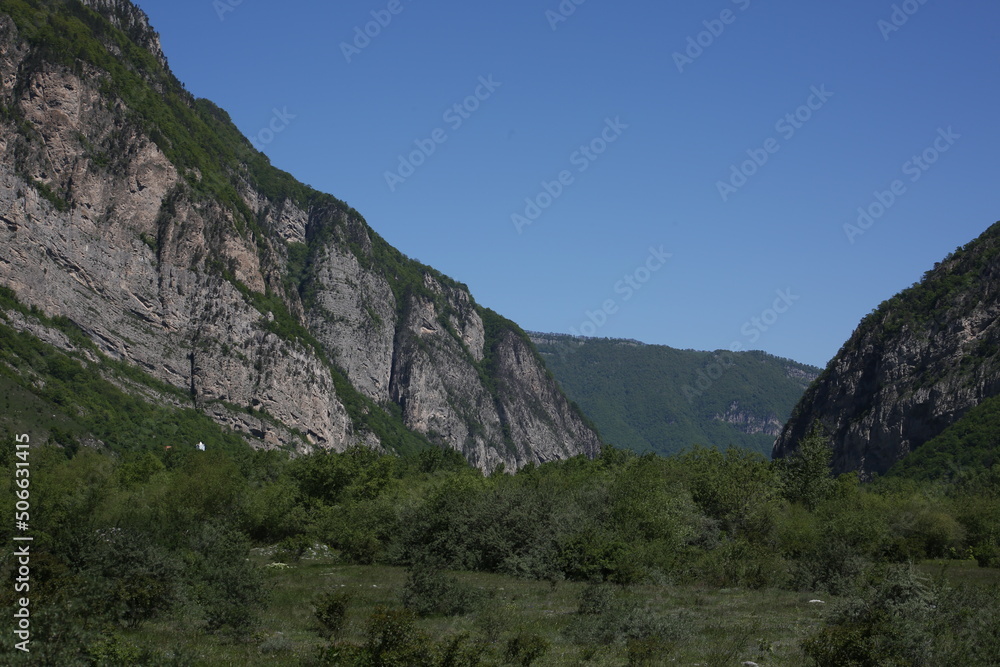 Caucasian mountains in sunny weather, green dense forests on the mountains and snowy peaks of the old high mountains of Georgia