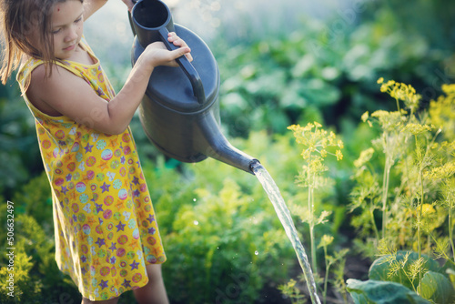 Fotografia cute kid girl with big watering can waters beds in garden in summer, helping children in garden and child taking care of plants