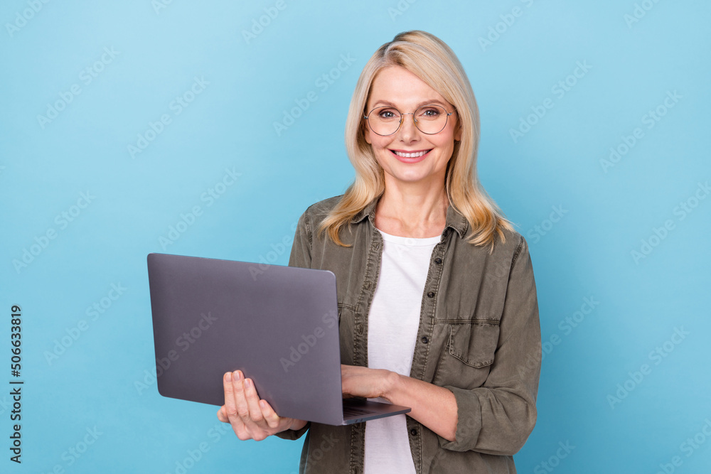 Photo of aged marketer lady hold netbook ready consult online partners wear khaki shirt isolated blue color background Photo of aged marketer lady hold netbook ready consult online partners wear khaki shirt isolated blue color background
