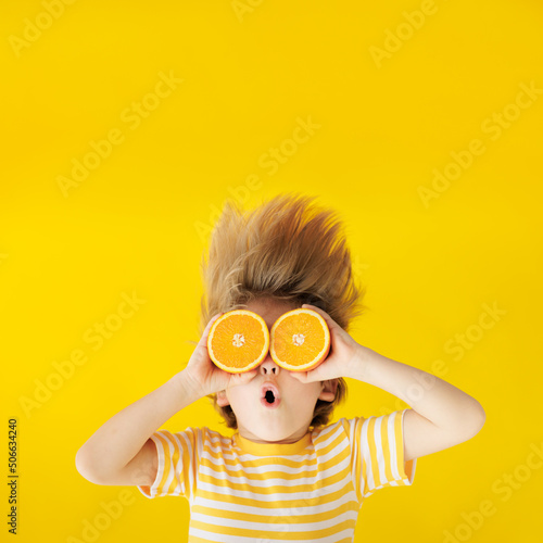 Surprized child holding slices of orange fruit like sunglasses