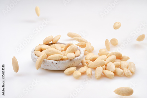 Pile of peeled or blanched almonds. Falling blanched Almonds. White bowl of peeled whole almonds on white background. Shallow depth of field photo