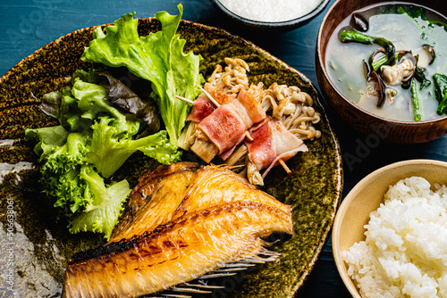 Grilled Atka mackerel set meal with rice, miso soup and salad against a blue plaster design board.  photo