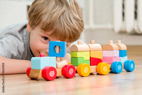 Fotografia Boy sitting on the floor and playing with wooden colorful block train