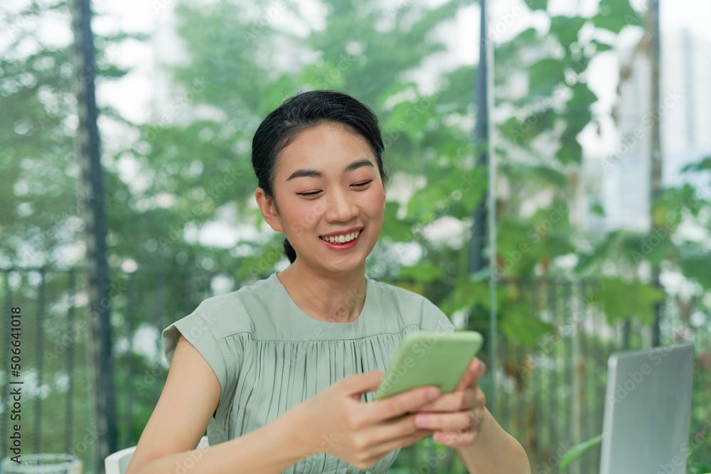 Happy young elegant businesswoman scrolling in smartphone while enjoying break by workplace