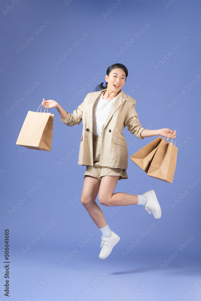 Woman carrying shopping bags and jumping on a purple background Woman carrying shopping bags and jumping on a purple background