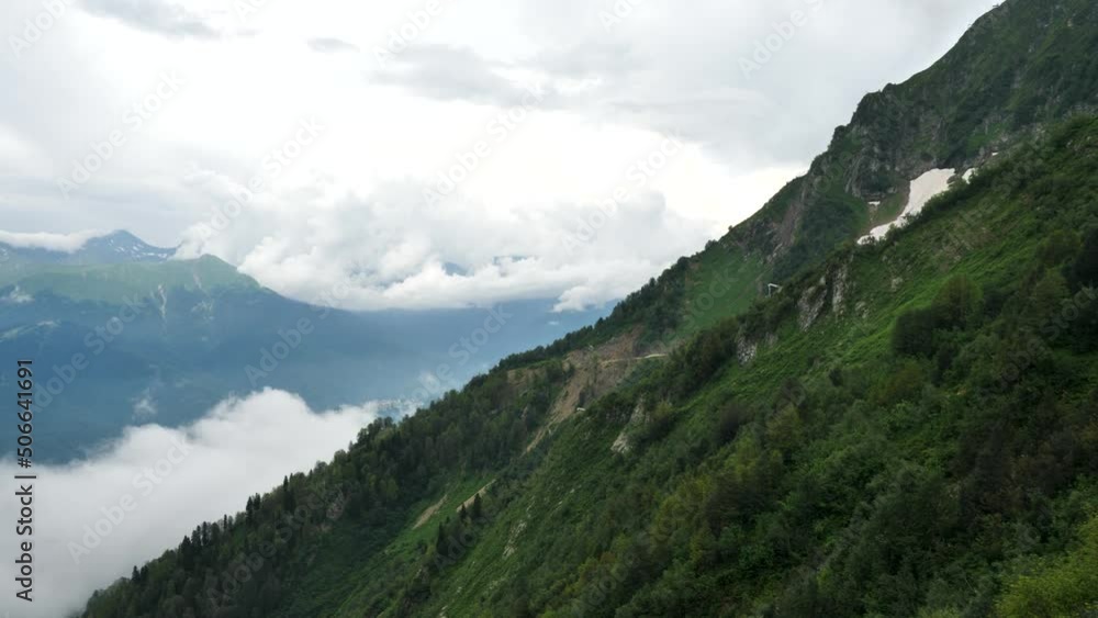 Drone rises up next to green mountains, clouds in mountains Drone rises up next to green mountains, clouds in mountains