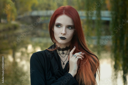 beautiful fashionable young girl witch model stands outdoors in the forest in autumn by the river, pale, vampire, goth