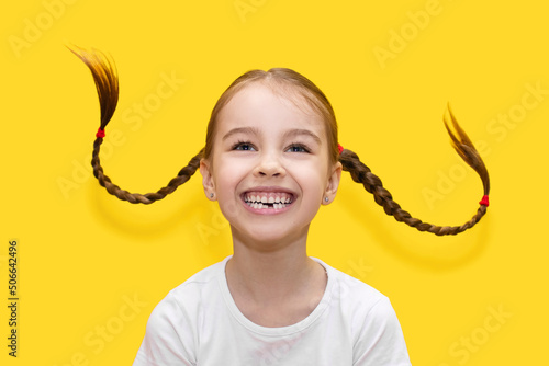 Canvastavla Cheerful child girl with growing teeth throws pigtails and laughs on a yellow background