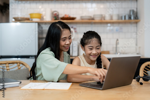 Mother teaching children to do their homework at home. Happy asian family using the laptop together at home. Young asian family parents helping daughter drawing at home © Natee Meepian