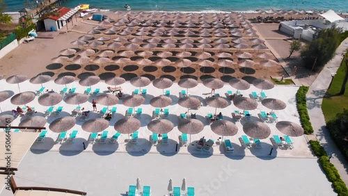 Flight over the beach with sun umbrellas towards the pool in a luxury hotel around of stone mountains on a warm sunny day