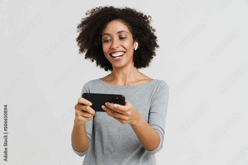 Young black woman in earphones smiling and using mobile phone Young black woman in earphones smiling and using mobile phone
