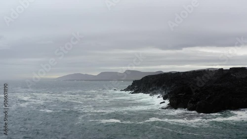 Black volcanic sea cliffs being hit by waves shot from drone in Iceland. photo