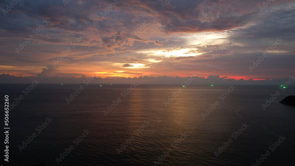 The red-orange sunset is reflected with clouds in the sea. An island can be seen in the distance. Smooth water is like a mirror. There is a lonely island. Not far from the shore of the boat. Epic