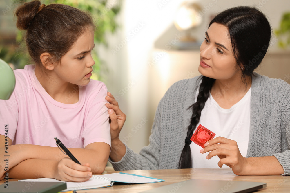 Mother talking with her teenage daughter about contraception while she doing homework at home. Sex education concept Mother talking with her teenage daughter about contraception while she doing homework at home. Sex education concept