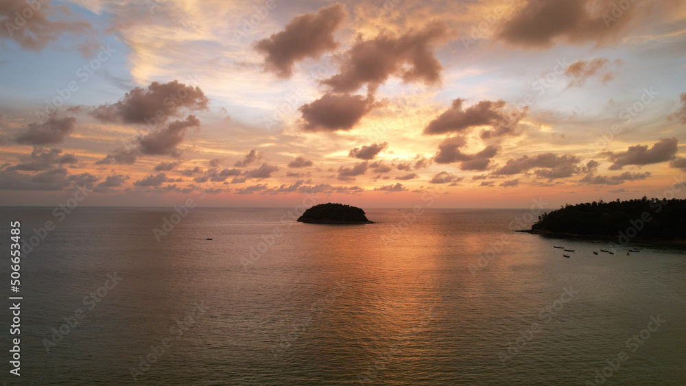 An epic orange sunset with a view of the island and clouds. A boat is sailing. The ocean reflects the color of the sky and clouds. Clouds shimmer with lilac-orange color. A lonely island in distance An epic orange sunset with a view of the island and clouds. A boat is sailing. The ocean reflects the color of the sky and clouds. Clouds shimmer with lilac-orange color. A lonely island in distance