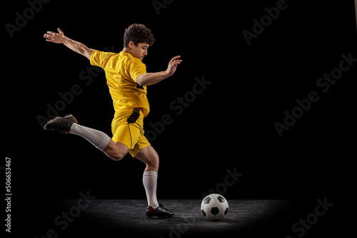 Dynamic portrait of professional football  soccer player training with ball isolated on dark background. Concept of sport  match  active lifestyle  goal and hobby