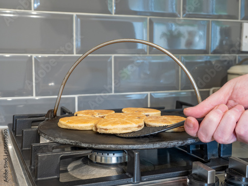chef turning Welsh Cake over whilst cooking on a cast iron griddle over a gas hob flame