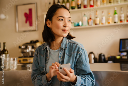 Canvas-taulu Young asian woman wearing denim shirt smiling and using mobile phone