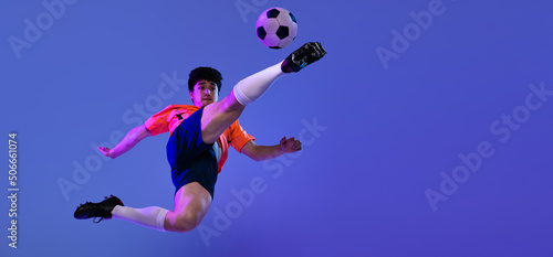 Studio shot of male professional football, soccer player practicing with ball isolated on purple background. Concept of sport, match, active lifestyle, goal and hobby © master1305