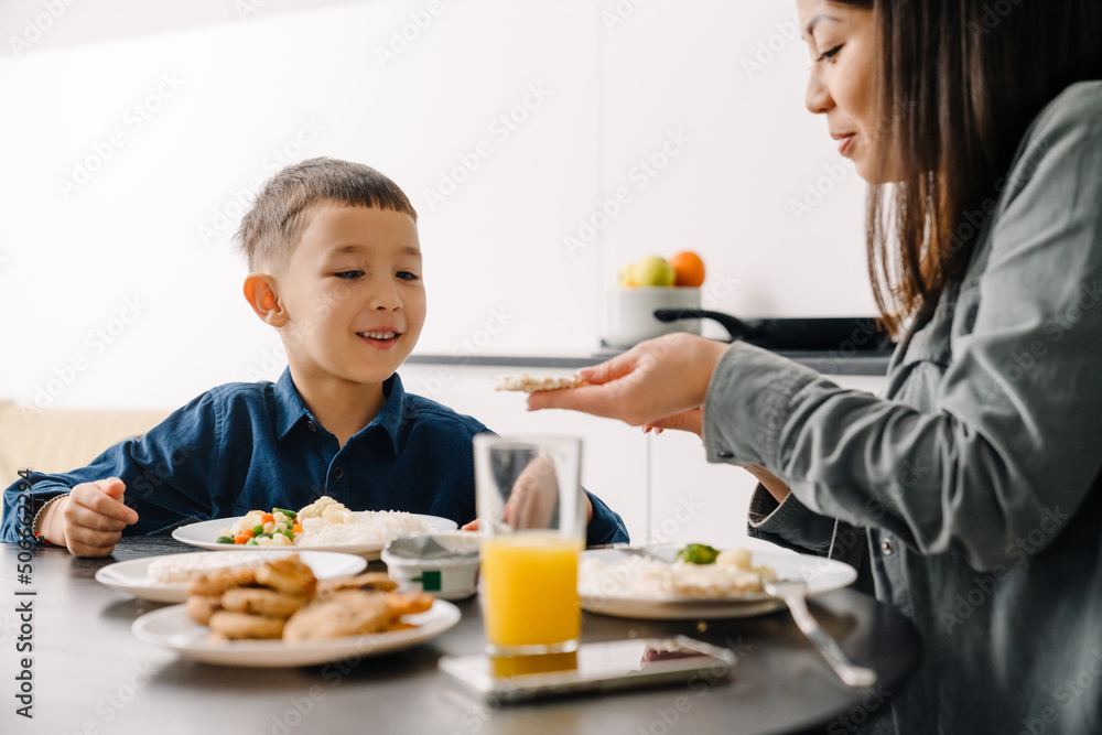 Asian woman and her son sitting at table having breakfast at home Asian woman and her son sitting at table having breakfast at home
